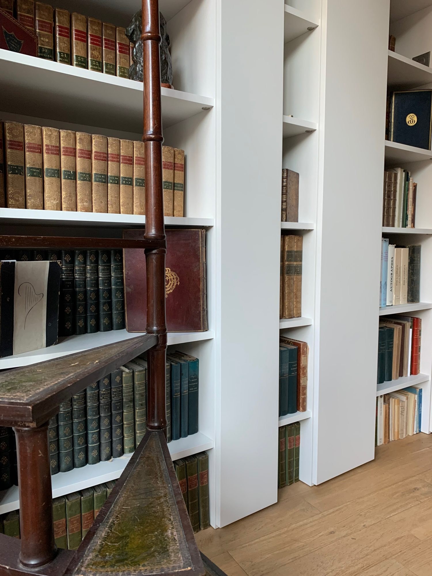 Bibliothèque aux étagères blanches garnies de livres anciens et escalier à colimaçon en acajou