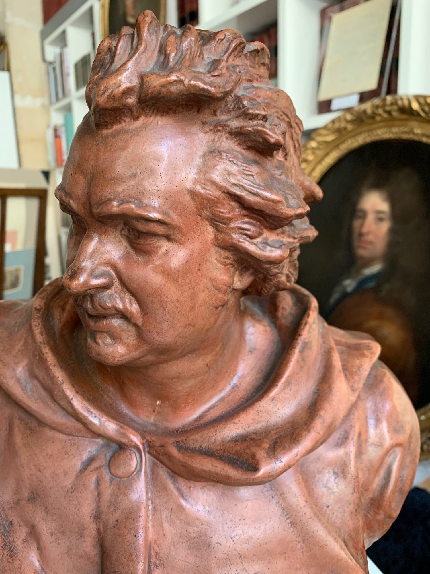 Buste en terre cuite d’un écrivain en robe à capuche devant un portrait ancien